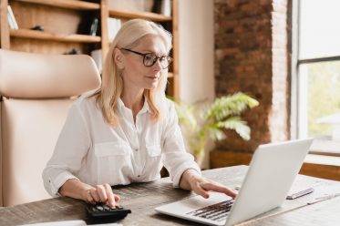 Middle-aged mature businesswoman boss financial advisor counting on calculator funds, money, paying domestic bills, debts, credit loan using laptop in office