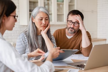 Financial advisor lawyer consulting mature middle-aged couple showing them debts, bunkruptcy, negative test results, mortgage, divorce certificate contract pension at home indoors