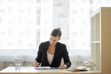 Front view of a pleasant young businesswoman or lawyer sitting at her office desk signing document or contract.